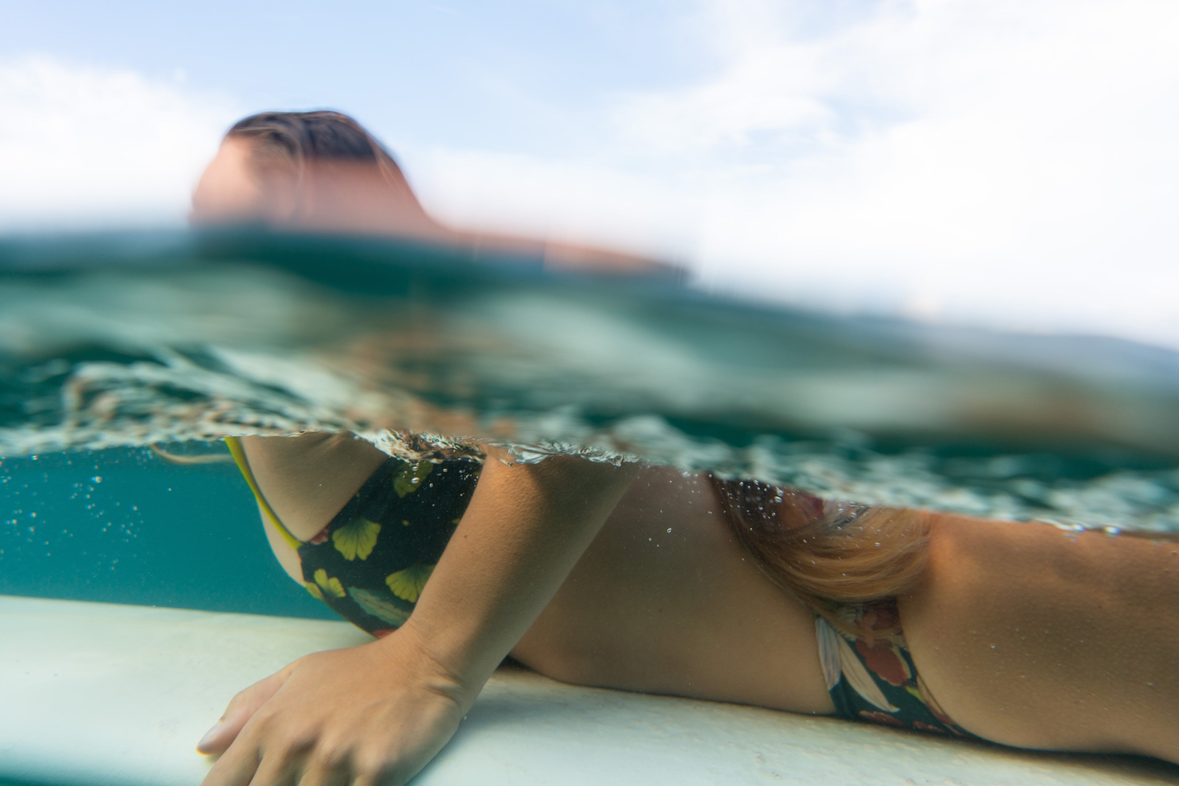 Woman lying on a surfboard with water and sky in the background